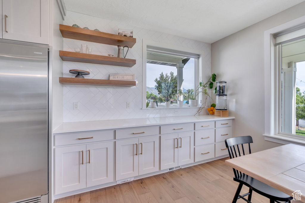 Kitchen with stainless steel fridge, backsplash, healthy amount of natural light, and light wood finished floors