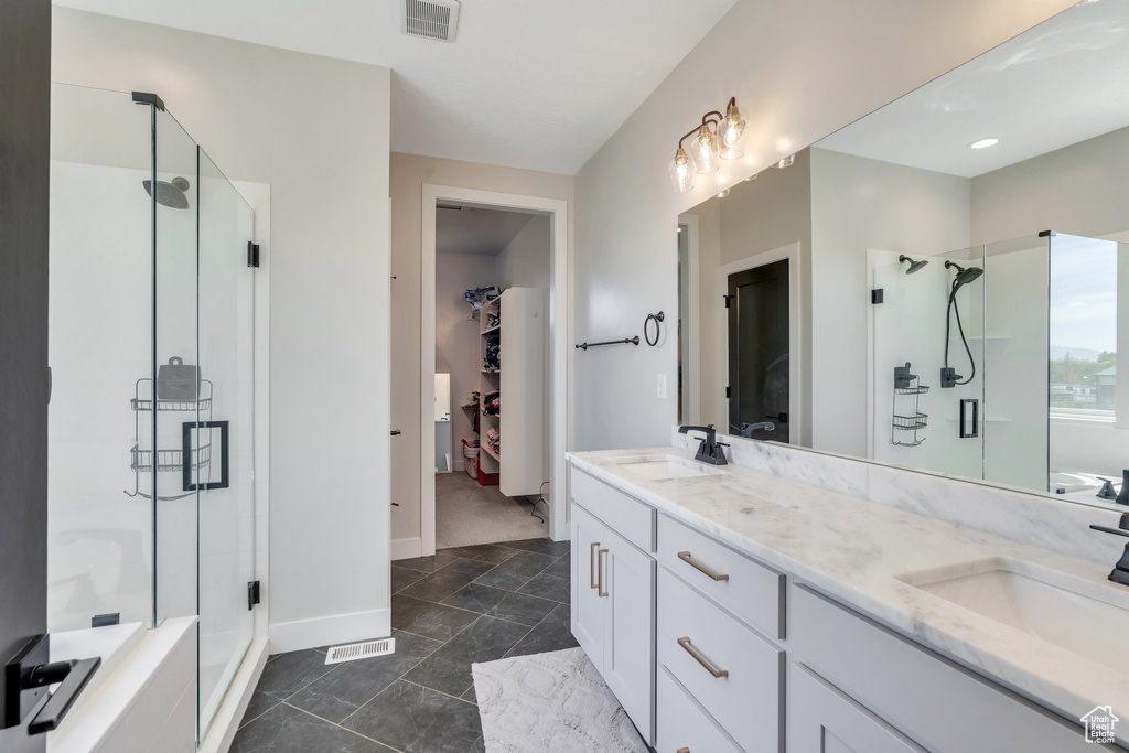 Bathroom featuring a stall shower, baseboards, double vanity, and a spacious closet