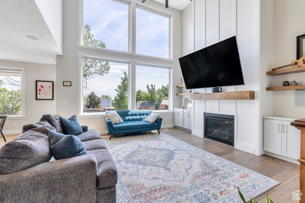 Living area with light wood-type flooring, a high ceiling, and a glass covered fireplace