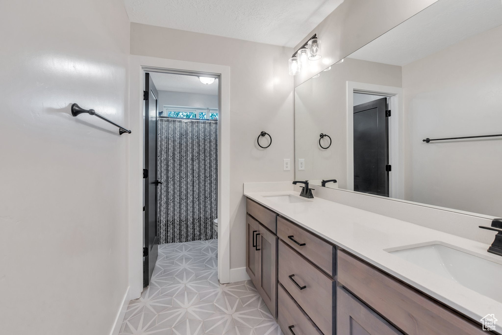 Bathroom featuring double vanity, toilet, baseboards, and curtained shower