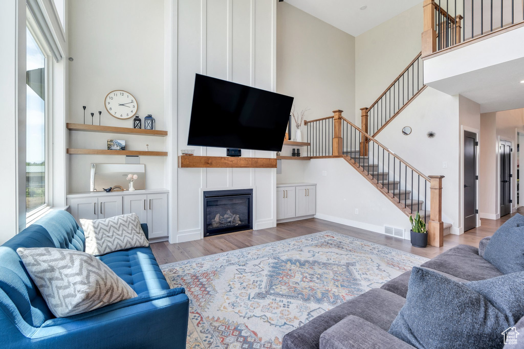 Living room with stairs, wood finished floors, a fireplace, and a towering ceiling