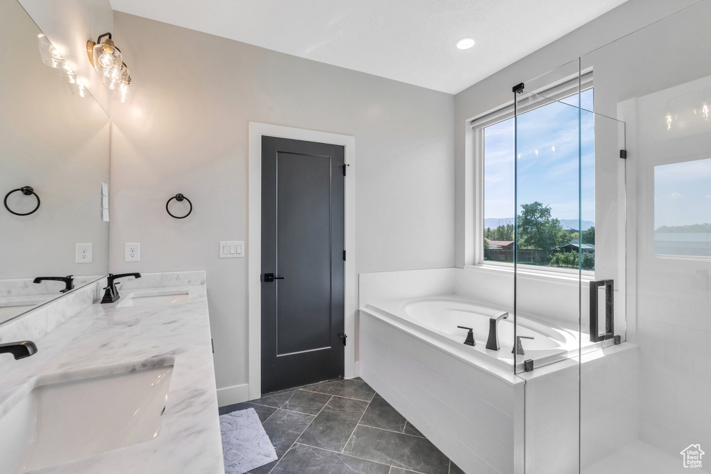 Full bath with marble look tiles, double vanity, a garden tub, and baseboards