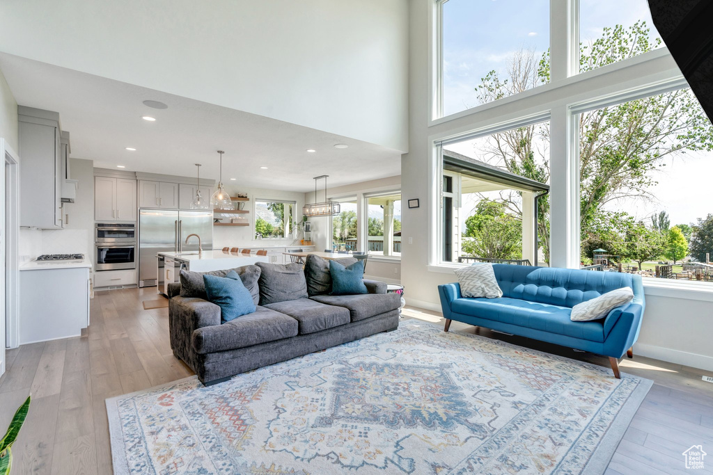Living room featuring light wood-style floors, a towering ceiling, baseboards, and recessed lighting
