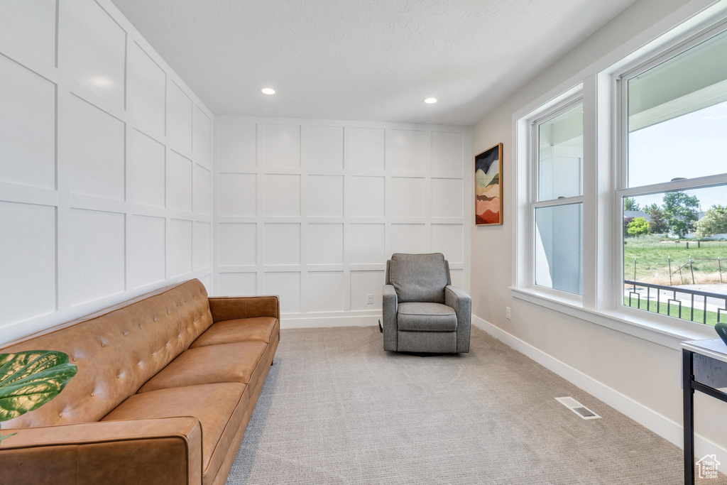 Living area with a decorative wall, recessed lighting, light carpet, and baseboards