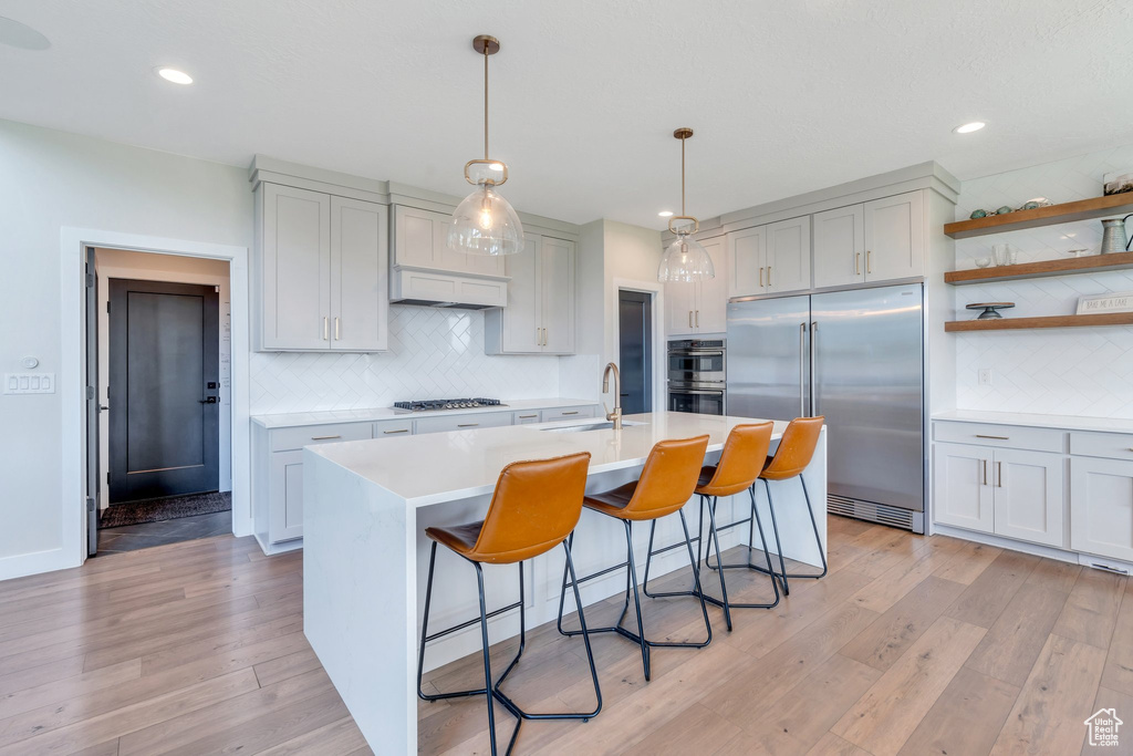 Kitchen with appliances with stainless steel finishes, light wood-style floors, light countertops, decorative backsplash, and a breakfast bar area