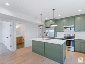 Kitchen with stainless steel appliances, green cabinetry, a sink, light wood-style floors, and light countertops