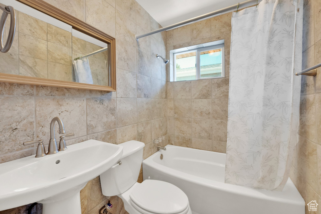 Bathroom with tile walls, a sink, shower / tub combo with curtain, and toilet