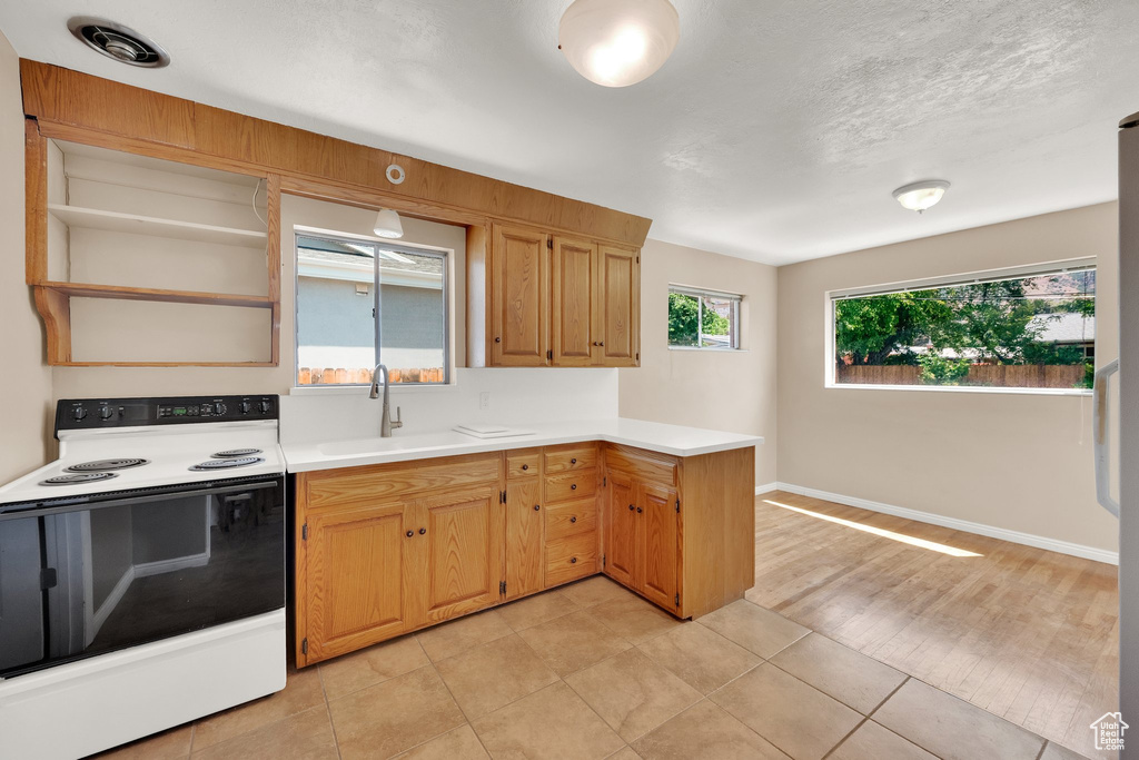 Kitchen featuring range with electric cooktop, a sink, open shelves, a peninsula, and light countertops