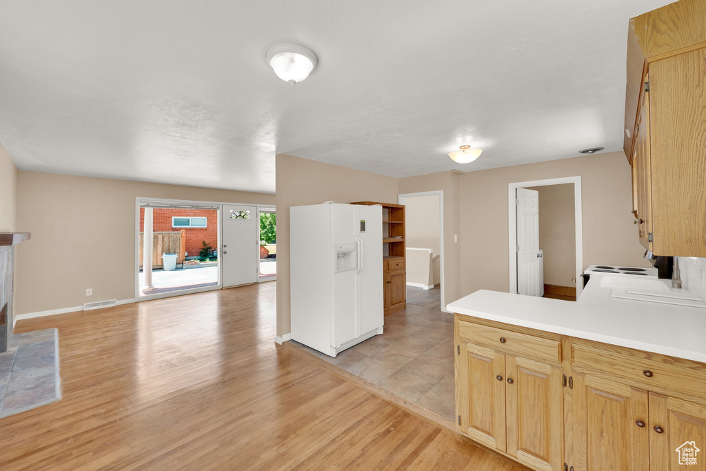 Kitchen with light wood-type flooring, light countertops, white fridge with ice dispenser, baseboards, and a peninsula