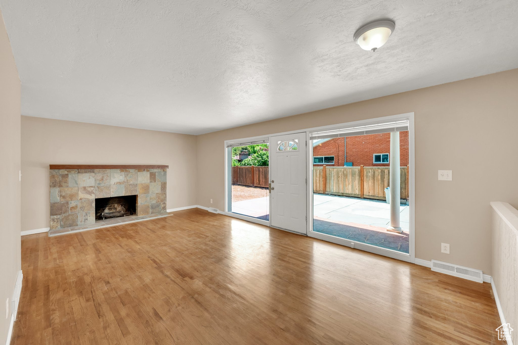 Unfurnished living room with wood finished floors, a fireplace, baseboards, and a textured ceiling
