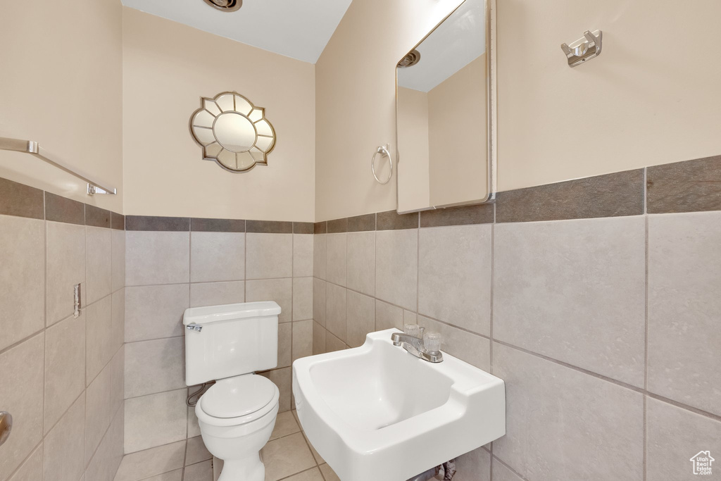 Bathroom featuring tile walls, toilet, a sink, and a wainscoted wall