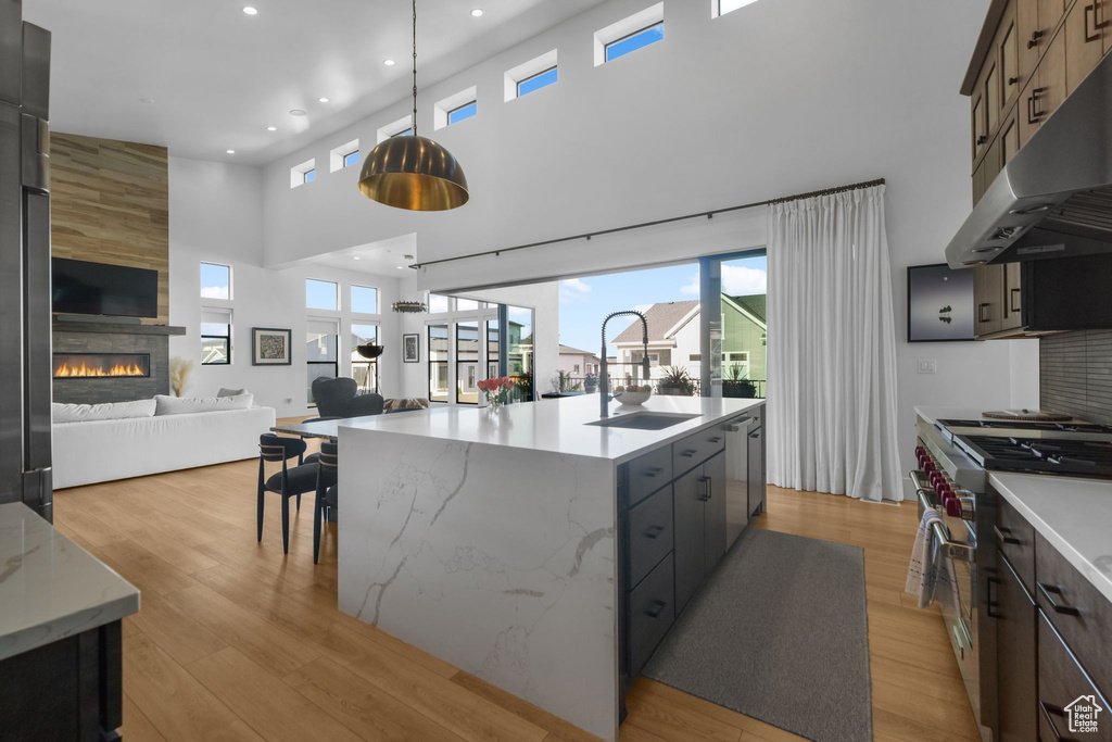 Kitchen with under cabinet range hood, appliances with stainless steel finishes, a towering ceiling, open floor plan, and a sink