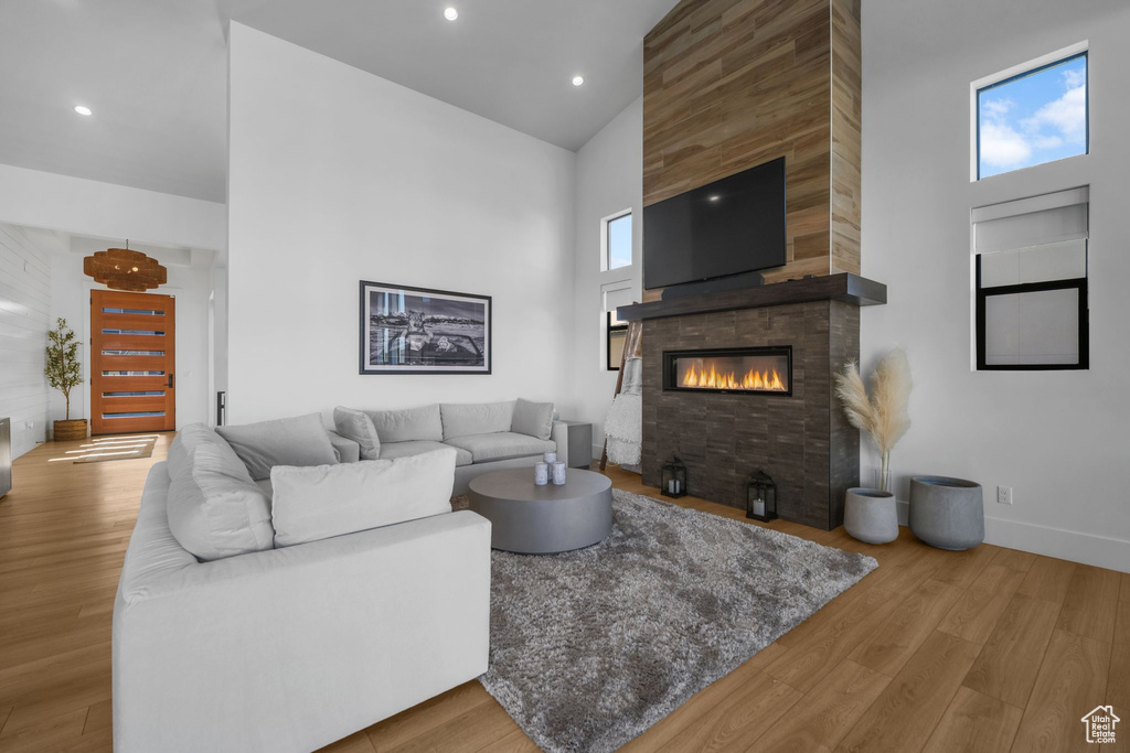 Living room featuring high vaulted ceiling, a tiled fireplace, wood finished floors, baseboards, and recessed lighting
