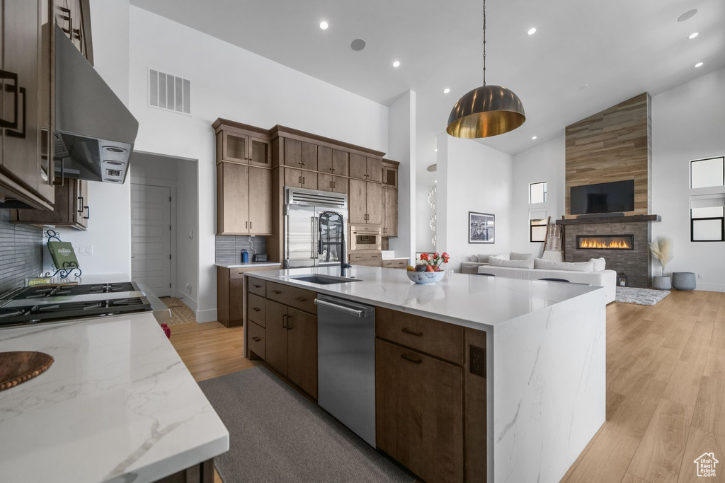 Kitchen with high vaulted ceiling, appliances with stainless steel finishes, range hood, open floor plan, and a sink