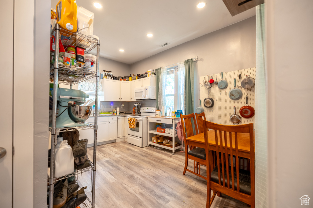 Kitchen with white appliances, white cabinetry, light countertops, light wood-style floors, and recessed lighting