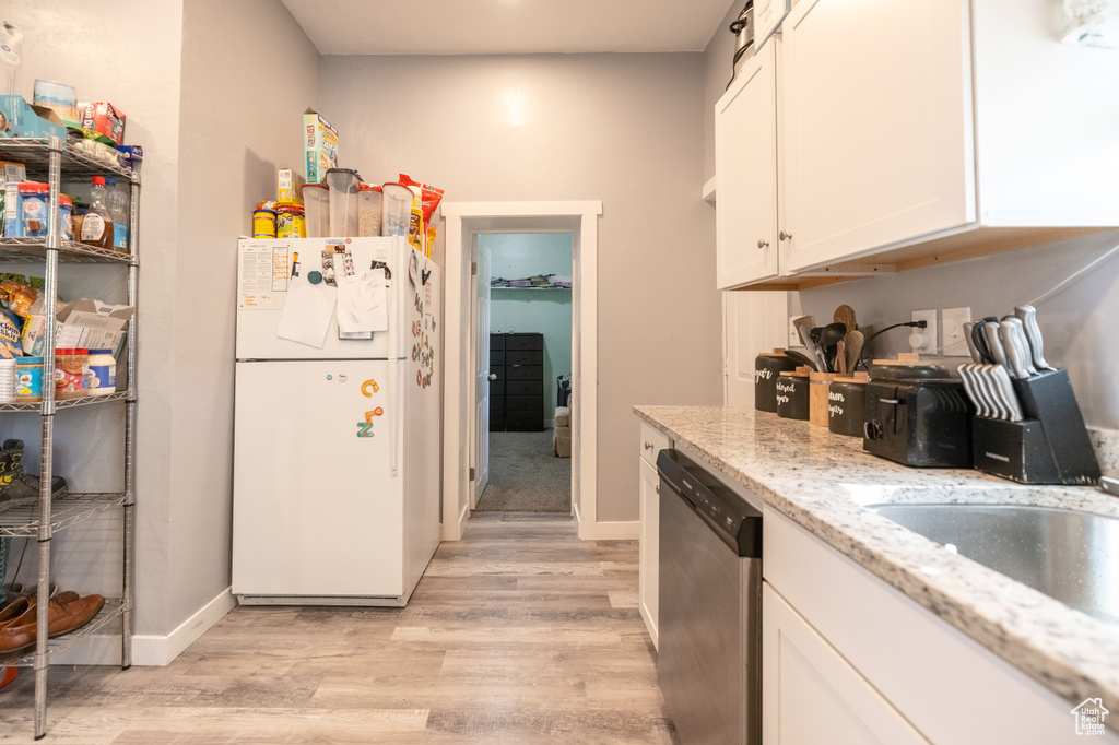 Kitchen featuring freestanding refrigerator, stainless steel dishwasher, light wood-style flooring, white cabinets, and light stone countertops