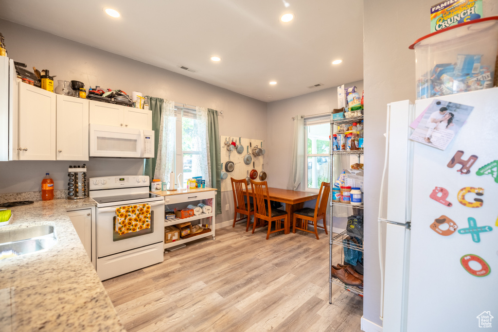Kitchen featuring white appliances, light wood-style floors, recessed lighting, healthy amount of natural light, and white cabinetry