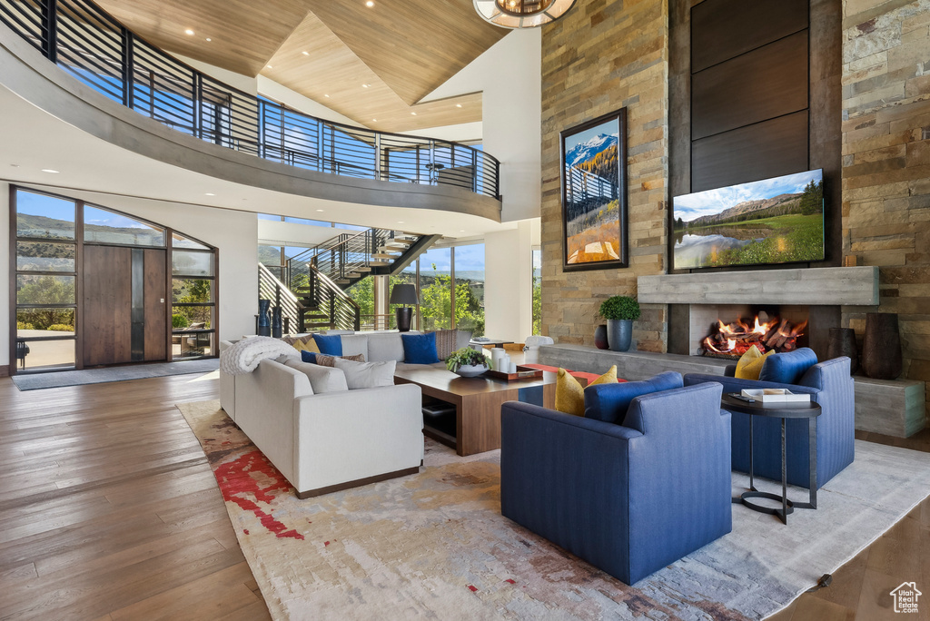 Living room featuring a towering ceiling, an outdoor stone fireplace, wooden ceiling, wood-type flooring, and recessed lighting