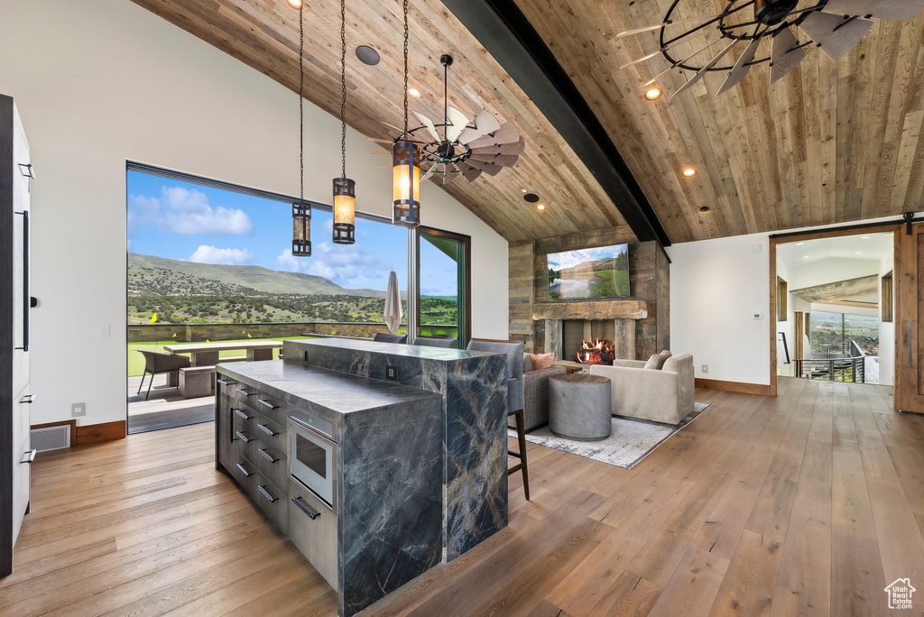Living area featuring baseboards, light wood finished floors, a stone fireplace, a ceiling fan, and high vaulted ceiling