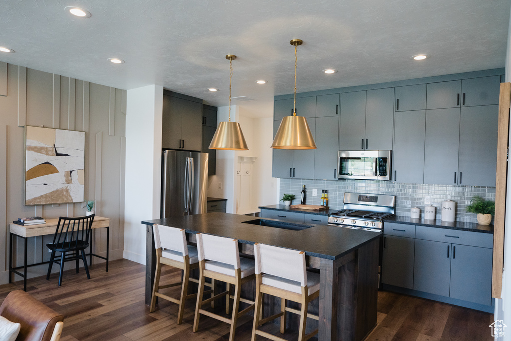 Kitchen with appliances with stainless steel finishes, dark countertops, dark wood-style flooring, a center island with sink, and recessed lighting