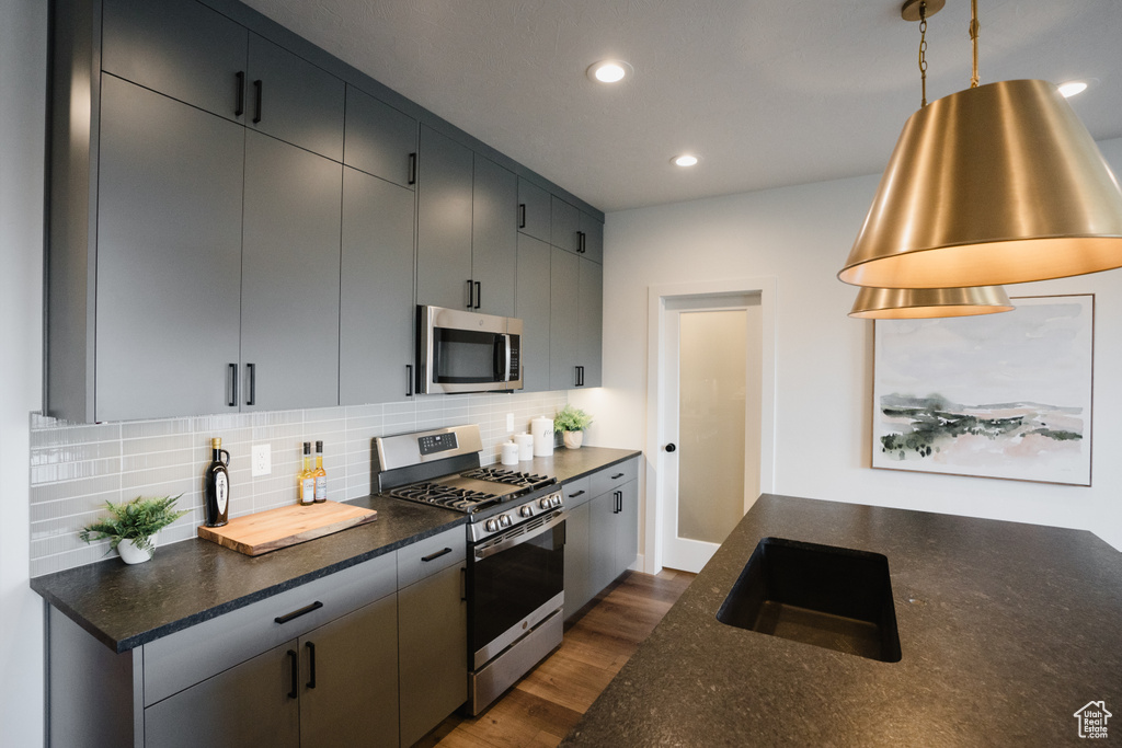 Kitchen featuring appliances with stainless steel finishes, a sink, backsplash, dark wood-style flooring, and recessed lighting