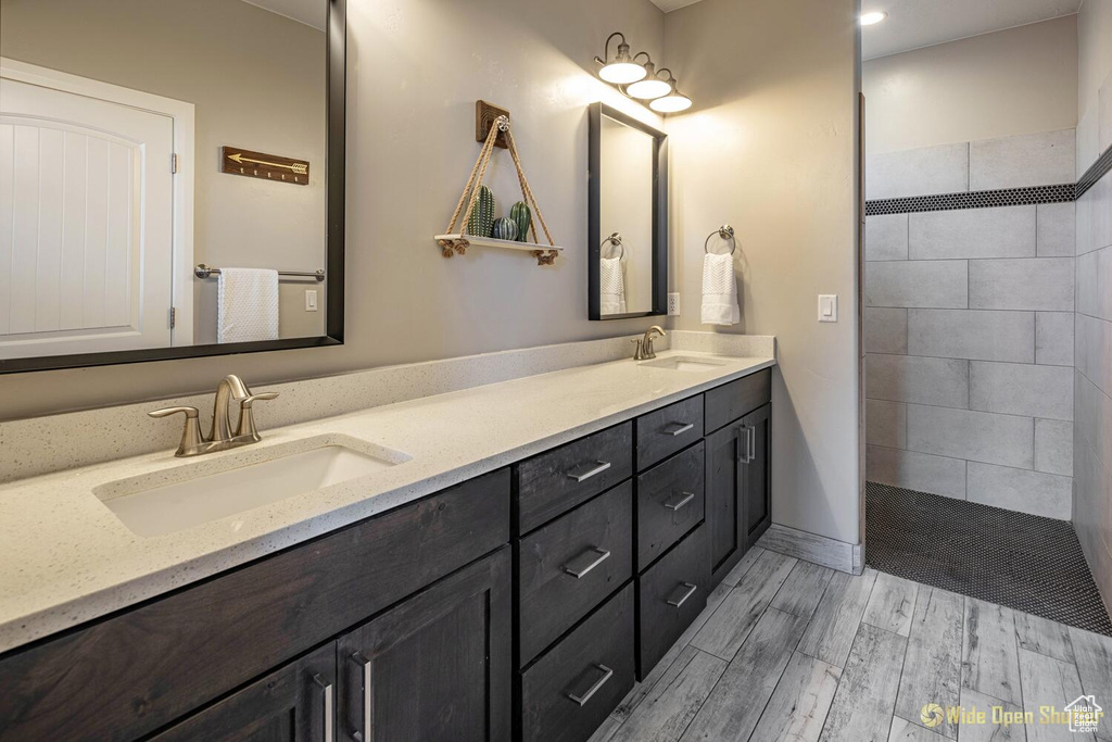 Bathroom featuring double vanity, a walk in shower, wood finished floors, and baseboards