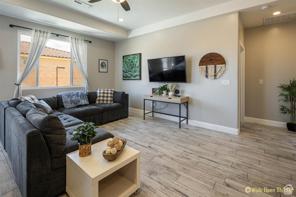 Living area with light wood-type flooring, a ceiling fan, baseboards, a tray ceiling, and recessed lighting