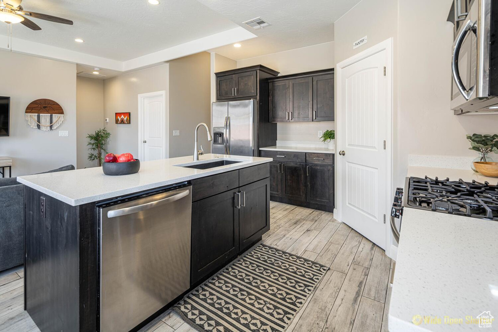 Kitchen featuring appliances with stainless steel finishes, a sink, light countertops, ceiling fan, and open floor plan