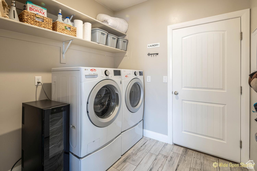 Laundry room with washing machine and clothes dryer, wine cooler, light wood-style flooring, and baseboards