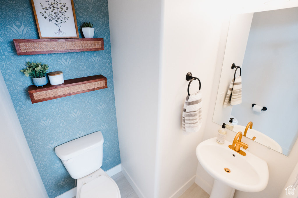 Half bath featuring toilet, wallpapered walls, and a sink