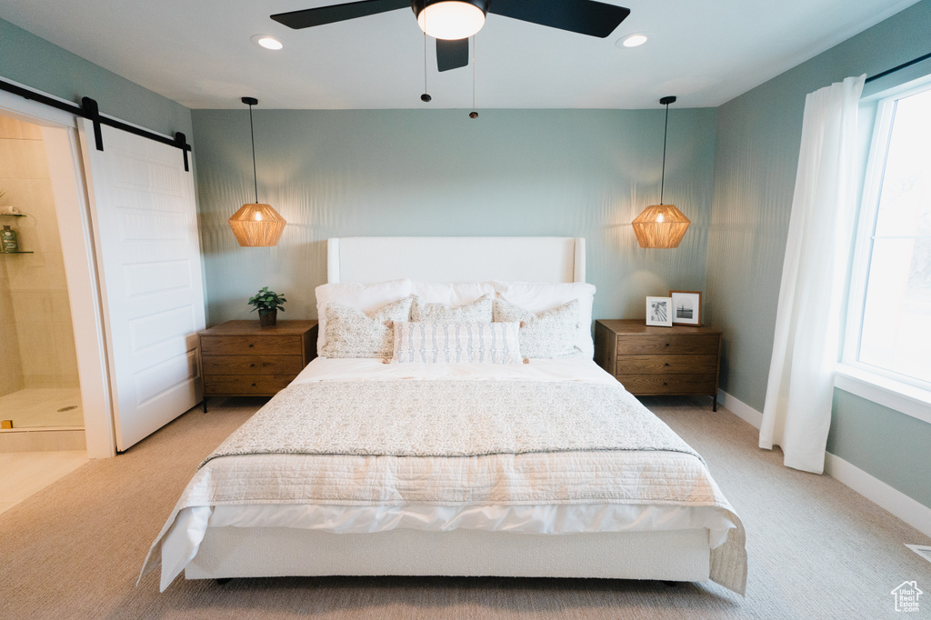 Bedroom featuring a barn door, light colored carpet, ceiling fan, baseboards, and ensuite bath