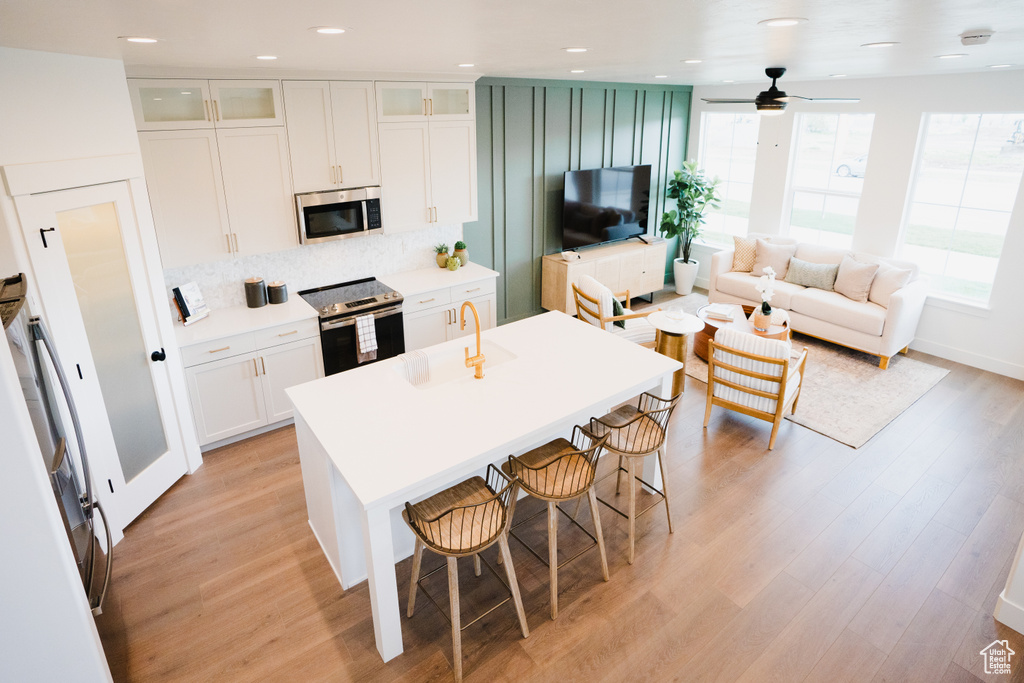 Kitchen featuring stainless steel appliances, a sink, a center island with sink, light wood-style flooring, and a ceiling fan