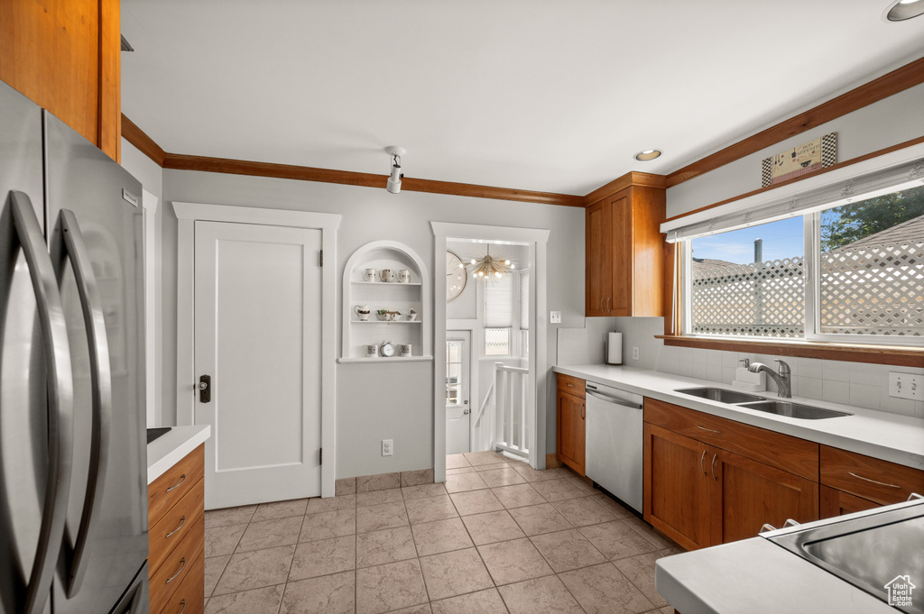 Kitchen featuring stainless steel appliances, a sink, light countertops, brown cabinetry, and tasteful backsplash