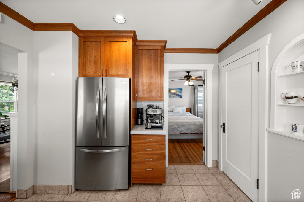 Kitchen with freestanding refrigerator, ornamental molding, brown cabinetry, light countertops, and ceiling fan