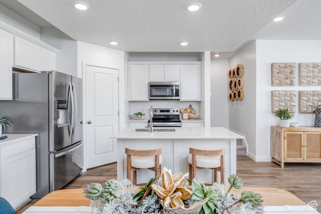 Kitchen with stainless steel appliances, light countertops, an island with sink, white cabinets, and recessed lighting