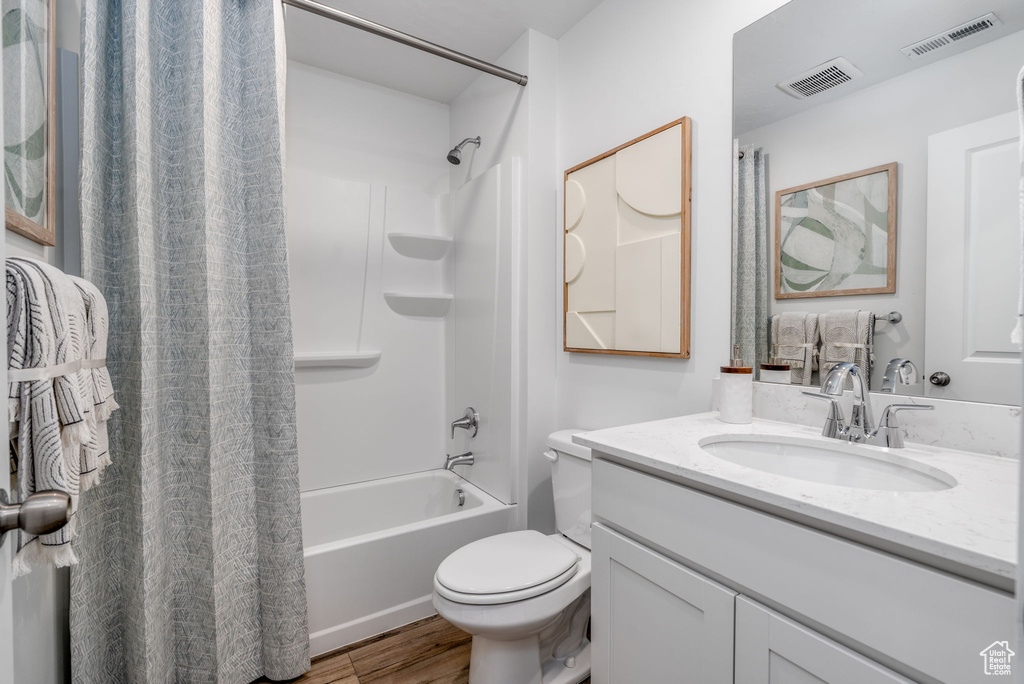 Bathroom featuring vanity, shower / bathtub combination with curtain, toilet, and wood finished floors
