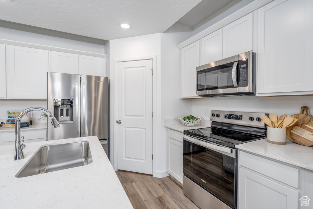 Kitchen with appliances with stainless steel finishes, a sink, white cabinets, light wood-style flooring, and recessed lighting