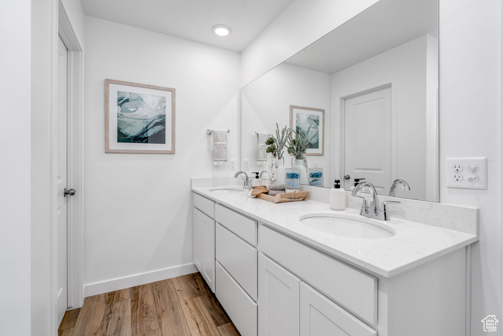 Bathroom featuring double vanity, wood finished floors, baseboards, and recessed lighting