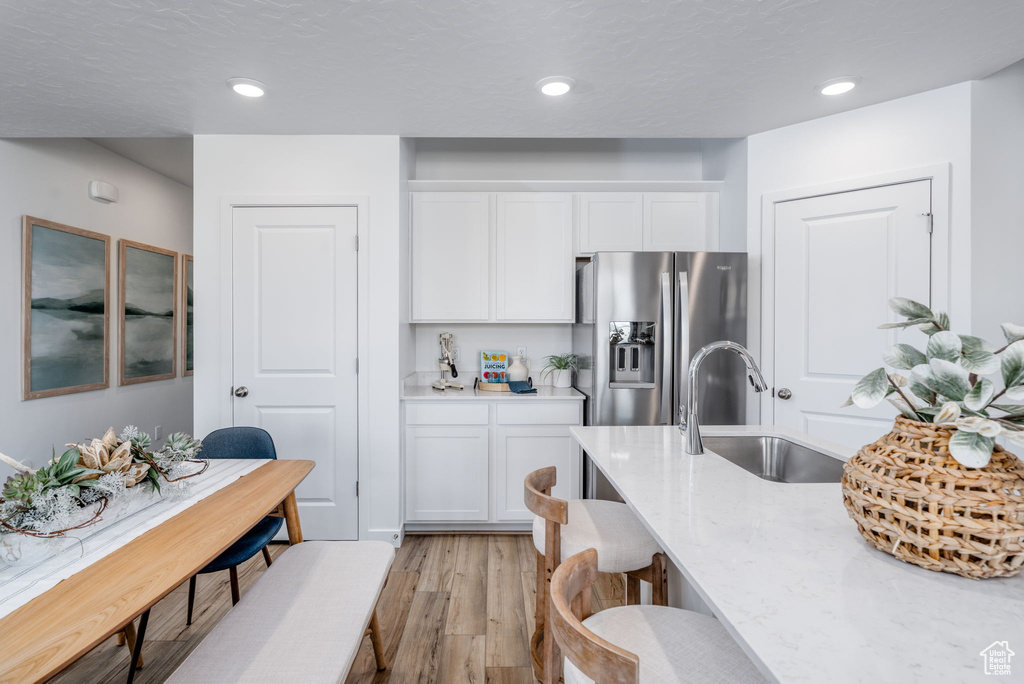 Kitchen with stainless steel fridge, a sink, light wood-type flooring, white cabinetry, and light stone countertops
