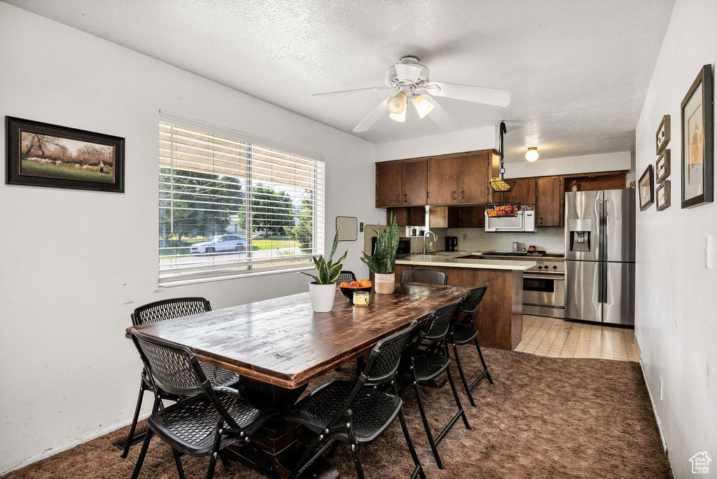 Dining space with ceiling fan, light colored carpet, and a textured ceiling
