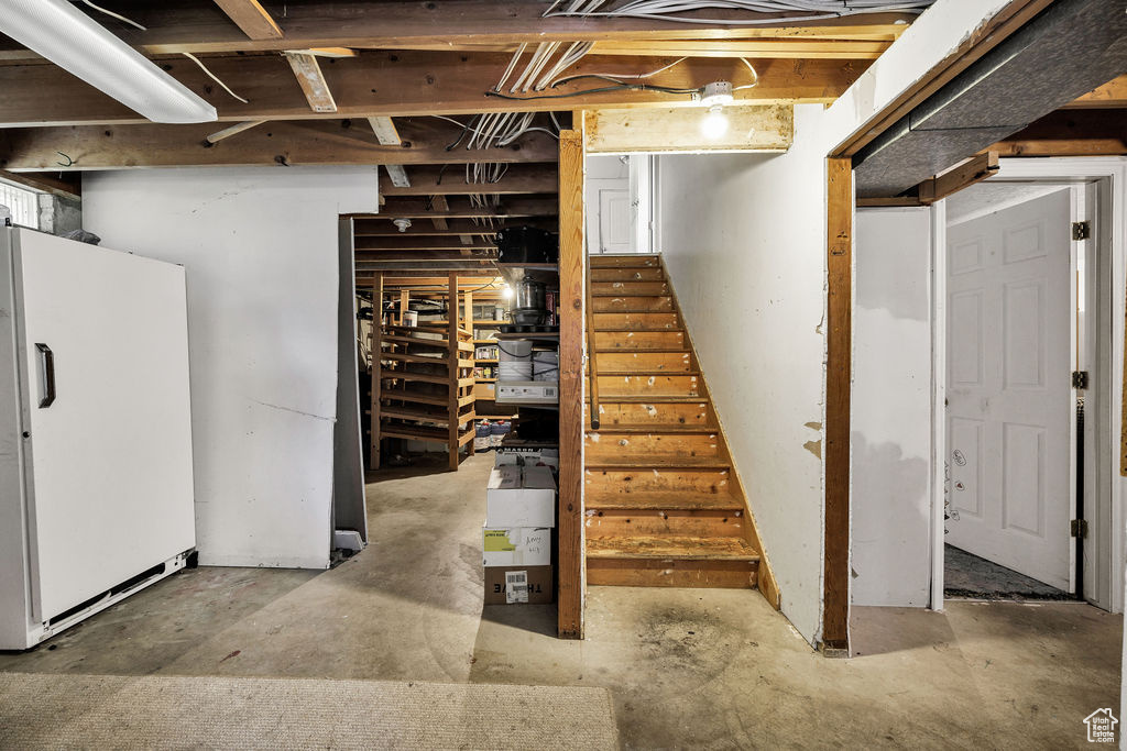Unfinished below grade area with freestanding refrigerator and stairway
