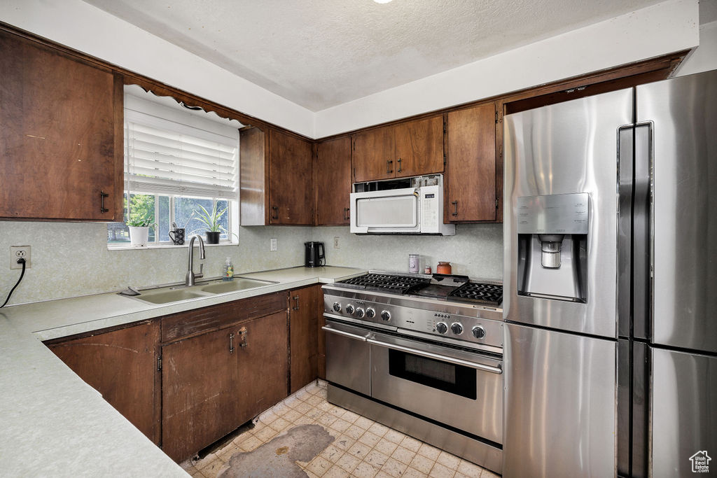 Kitchen with stainless steel appliances, a sink, light countertops, decorative backsplash, and light floors