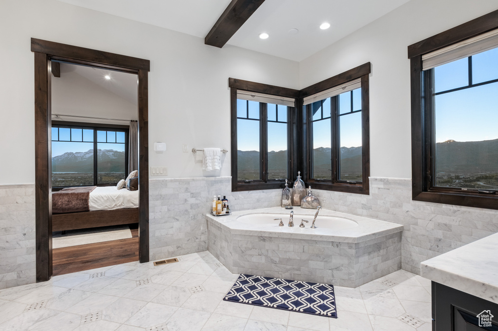 Ensuite bathroom with tile walls, plenty of natural light, a garden tub, a wainscoted wall, and vanity