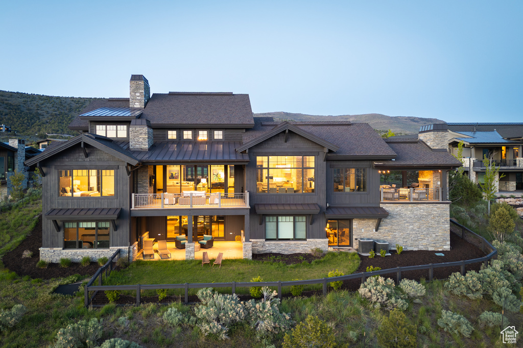 Rear view of house with a standing seam roof, a balcony, stone siding, and a chimney