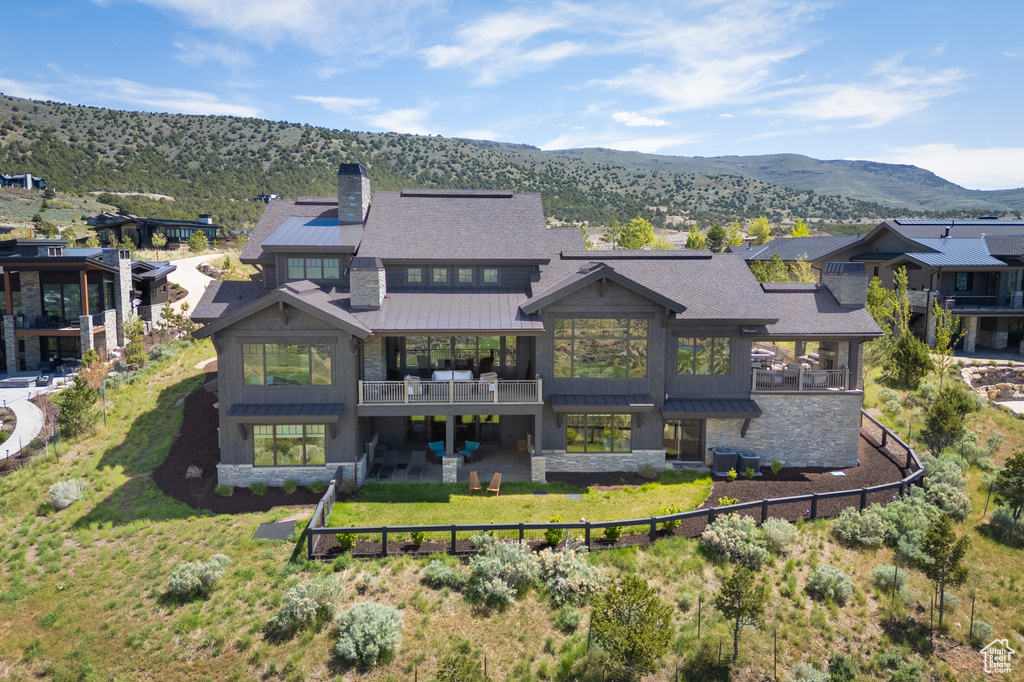 Back of house featuring a standing seam roof, a chimney, stone siding, and a fenced backyard