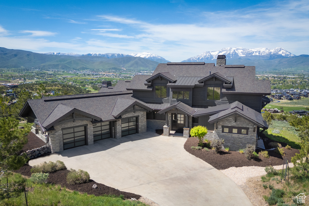 View of front facade with stone siding, a standing seam roof, a chimney, driveway, and an attached garage