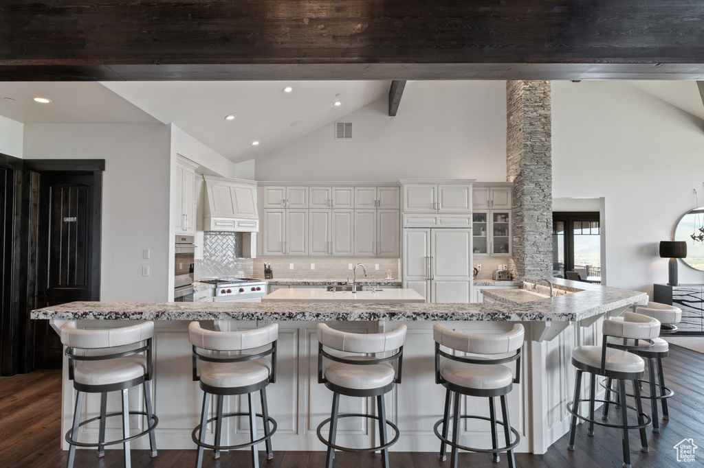 Kitchen with paneled fridge, decorative backsplash, dark wood-type flooring, a sink, and beam ceiling