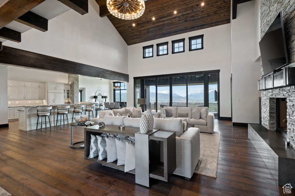 Living room with high vaulted ceiling, a stone fireplace, dark wood finished floors, baseboards, and beam ceiling