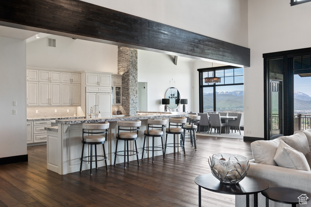 Kitchen with high vaulted ceiling, a kitchen bar, decorative backsplash, dark wood-style floors, and light stone counters
