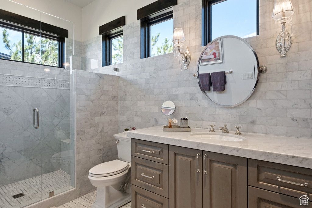 Bathroom with vanity, tile walls, toilet, a shower stall, and tile patterned floors
